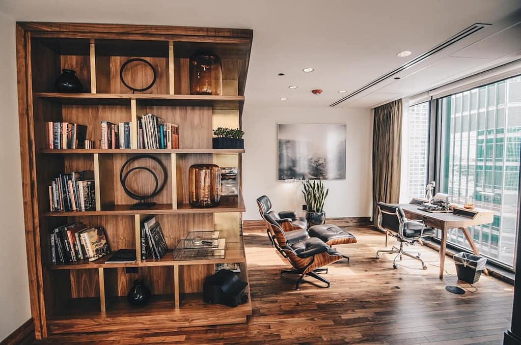 A home office with a wooden bookshelf and a big window.