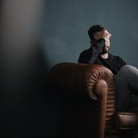 debt problem a man holds his head while sitting on a sofa