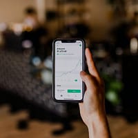 trading software person holding black iPhone displaying stock exchange