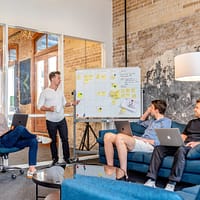 Event Planning Business three men sitting while using laptops and watching man beside whiteboard