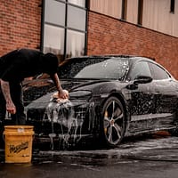 car shampoo man in black t-shirt and black pants doing water splash on black coupe during daytime