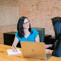 Leadership Coaching - woman in teal t-shirt sitting beside woman in suit jacket