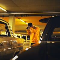 man holding cap standing between car on parking lot