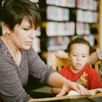 woman in gray long sleeve shirt sitting beside boy in orange crew neck shirt