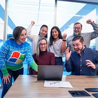 men and women sitting and standing by the table looking happy while staring at laptop