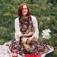 woman in white cardigan sitting on pink textile on green grass field during daytime