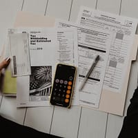 person holding paper near pen and calculator