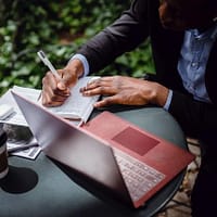 A woman entrepreneur writing something in her notebook and sitting in front of a laptop.