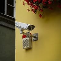 white and gray security camera mounted on yellow painted wall