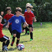 boy in red and blue soccer jersey kicking soccer ball on green grass field during daytime