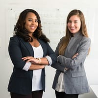 two women in suits standing beside wall