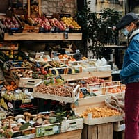 man in blue jacket standing in front of fruit stand