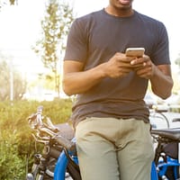 man holding smartphone leaning on bicycle during daytime