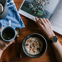 person holding blue ceramic mug and white magazine