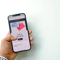 Close-up of a Man Holding a Smartphone Displaying a Shop with Airbnb Gift Cards