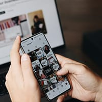 A person holding a cell phone in front of a laptop