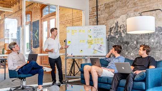 Event Planning Business three men sitting while using laptops and watching man beside whiteboard