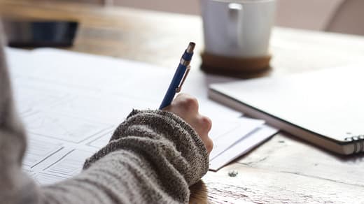 scholarship person writing on brown wooden table near white ceramic mug