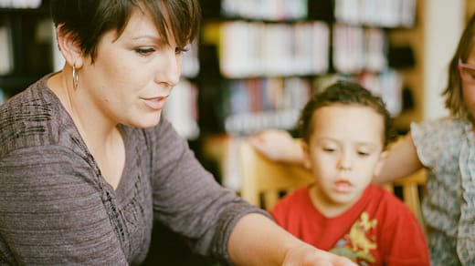 woman in gray long sleeve shirt sitting beside boy in orange crew neck shirt