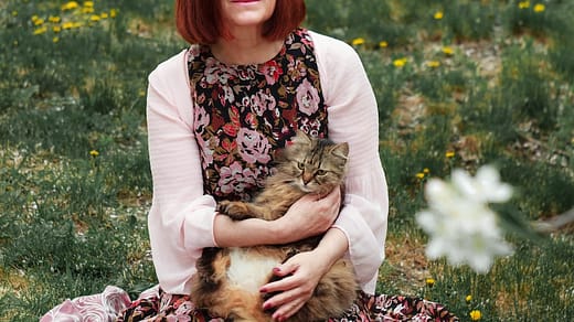 woman in white cardigan sitting on pink textile on green grass field during daytime