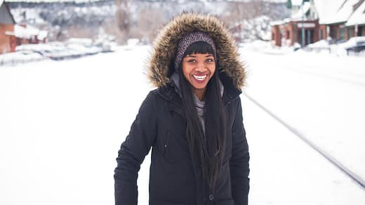 woman wearing coat standing on snow and smiling during daytime