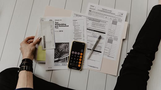 person holding paper near pen and calculator