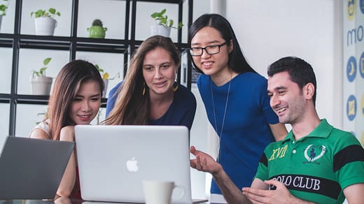 four people watching on white MacBook on top of glass-top table