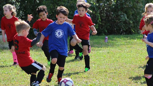 boy in red and blue soccer jersey kicking soccer ball on green grass field during daytime