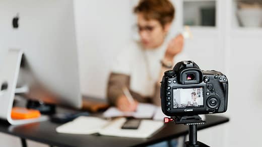 Unrecognizable blurred lady working at table in modern office against photo camera placed on tripod